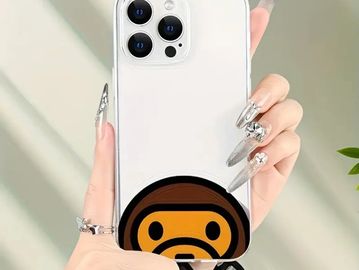 Hand holding a white iPhone with a monkey face sticker on the back.