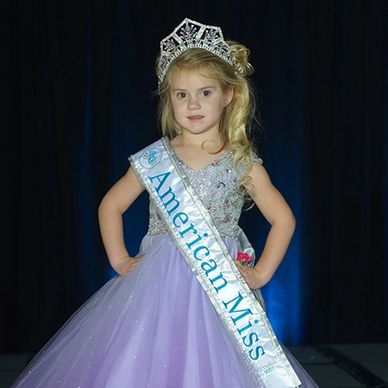 American Miss Mini wearing a lilac gown and her new AMP national crown and banner.