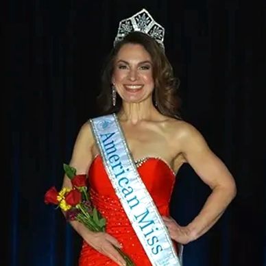 American Miss National Elegant Miss wearing a red satin gown with her AMP National crown and banner.