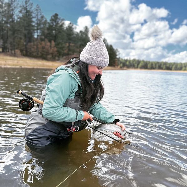 Woman fishing in a lake, holding a caught fish with a smile.