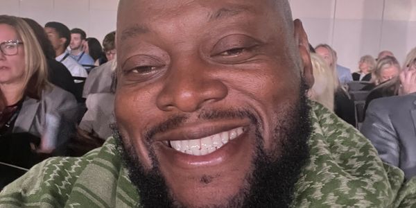Smiling man wearing a green patterned scarf at a conference.