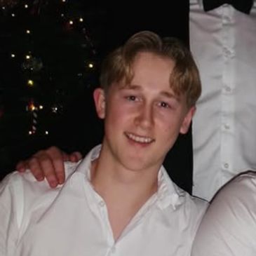 Young man smiling in a white shirt at a festive gathering.