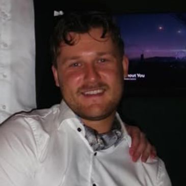 A man smiling in a white shirt with a hand on his shoulder.