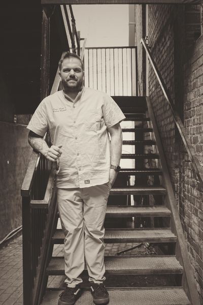 Man in medical scrubs leans on stair railing in an urban setting.