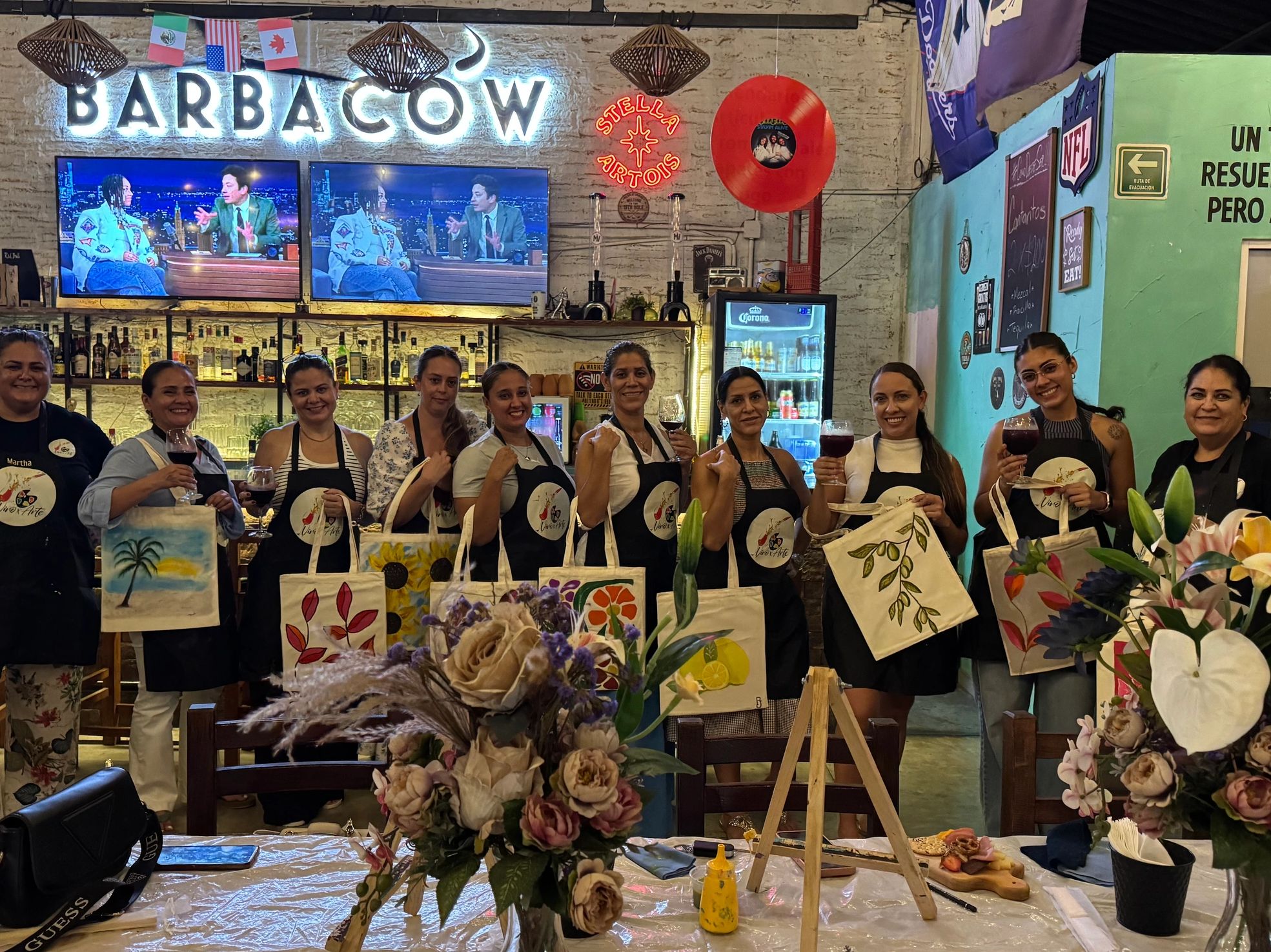 Mujeres sonrientes con vinos y bolsas pintadas en bar.