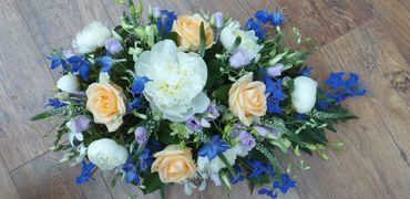A single ended spray for funerals. Featuring the white peony and pale peach & blue flowers