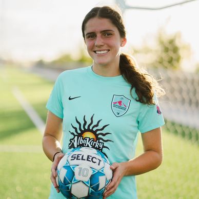 Smiling female soccer player holding a ball on the field.