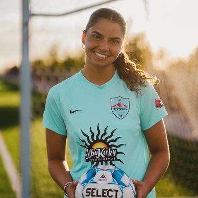 Smiling female soccer player holding a ball on a field.