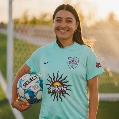 Woman soccer player smiling while holding a soccer ball.