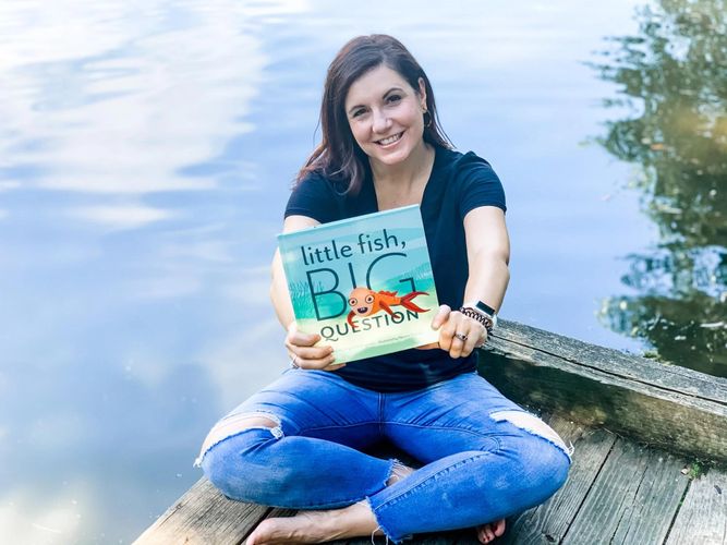 Author Angela Willingham sitting on a dock holding a copy of her book Little Fish, Big Question