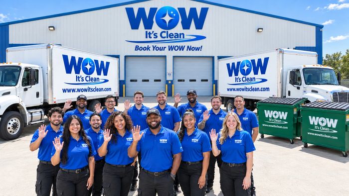 Group photo of WOW Its Clean staff in uniform waving with trucks and dumpsters.