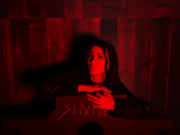 Woman in red light leaning on a wooden object with mysterious carvings.