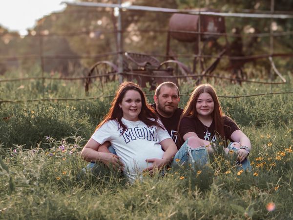 Pregnant mom with dad and teen daughter sitting in a field.