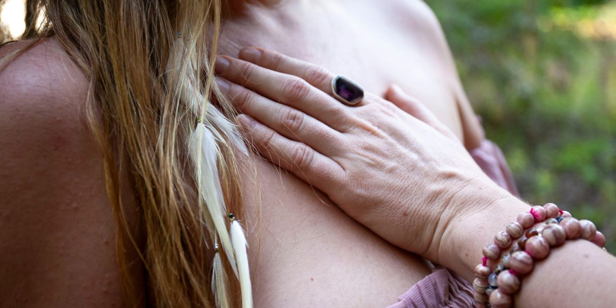 Hand with rings and bracelets resting on chest with feathered hair strand.