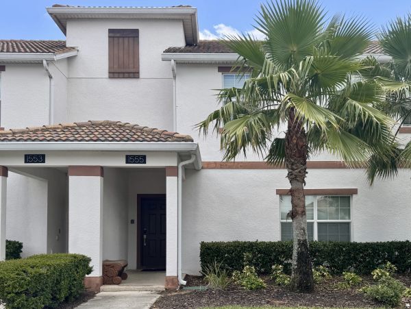 Front exterior of a two-story townhouse with a covered entry, white stucco exterior, tile roof, land