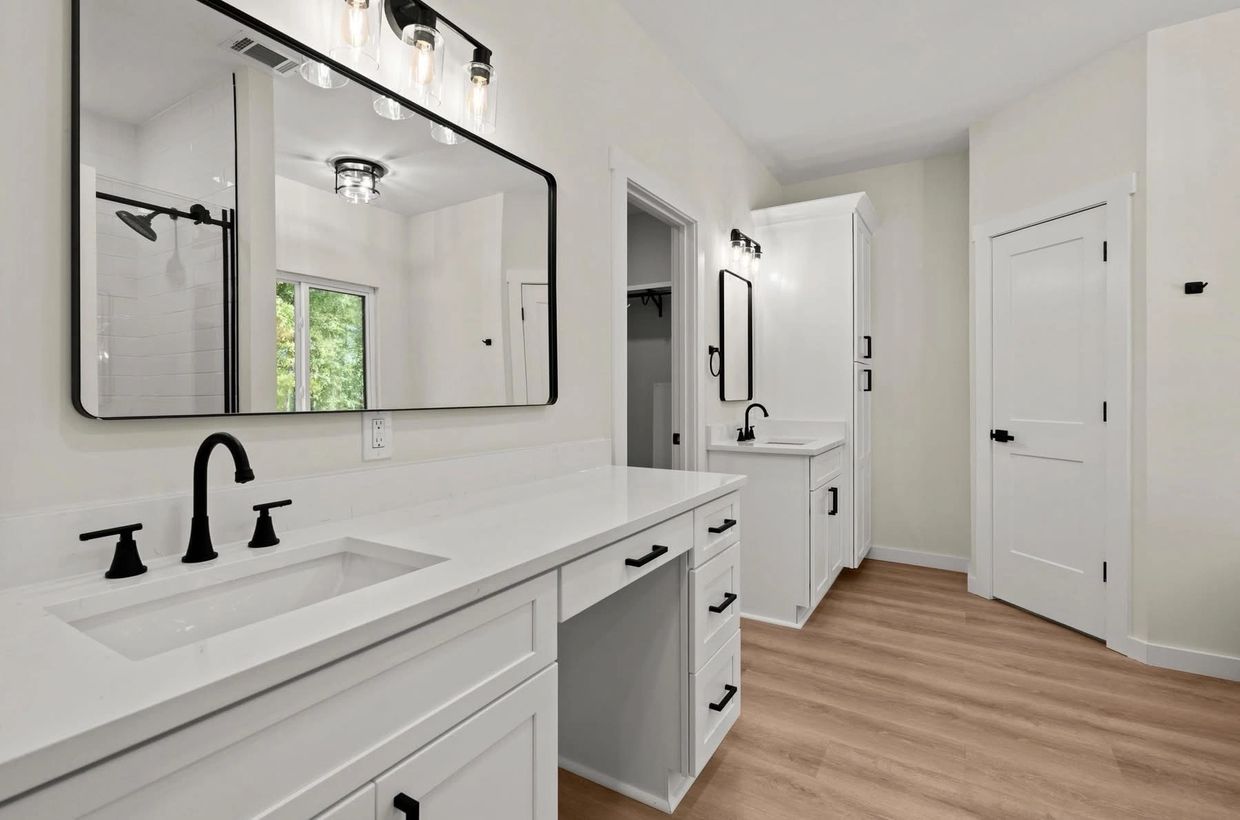 Modern white bathroom with black fixtures and wood flooring.