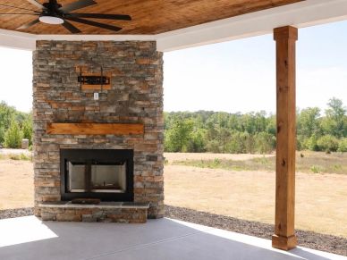 Outdoor stone fireplace with wooden mantel under covered patio.
