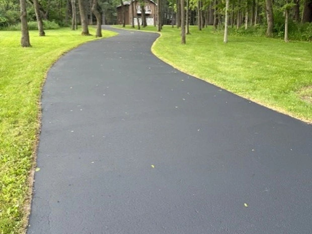 A freshly paved driveway winding through a green lawn and trees.