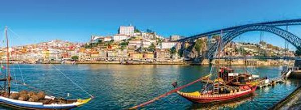 Scenic river view with colorful buildings and traditional boats under a large bridge.