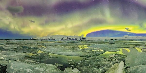 Aurora borealis glowing over icy Arctic landscape under starry sky.