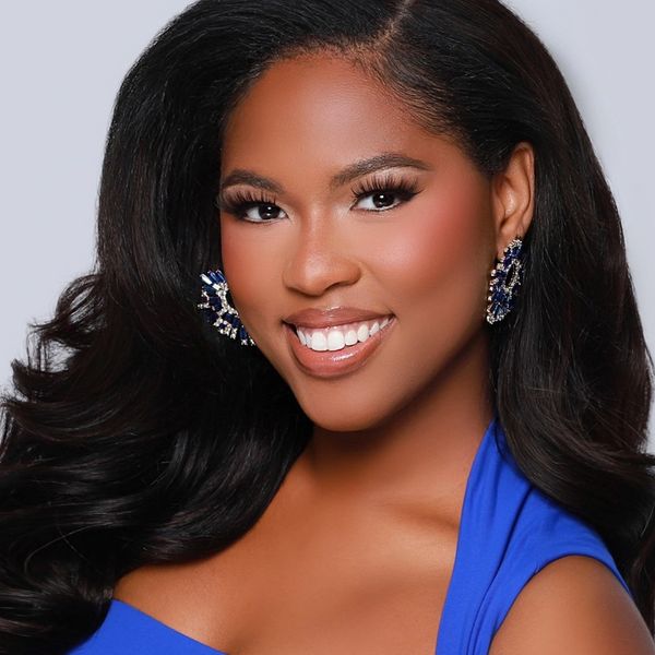 Woman smiling with elegant earrings and blue dress.