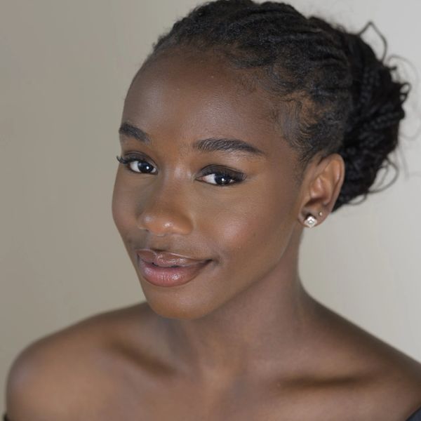 Close-up portrait of a smiling young woman with braided hair and natural makeup.
