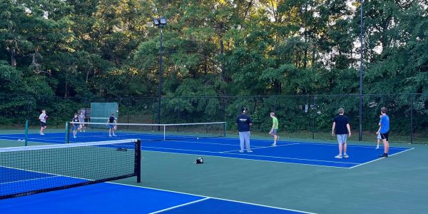 People playing tennis on outdoor courts surrounded by trees.
