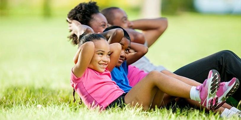 A family doing sit-ups together outdoors on grass.