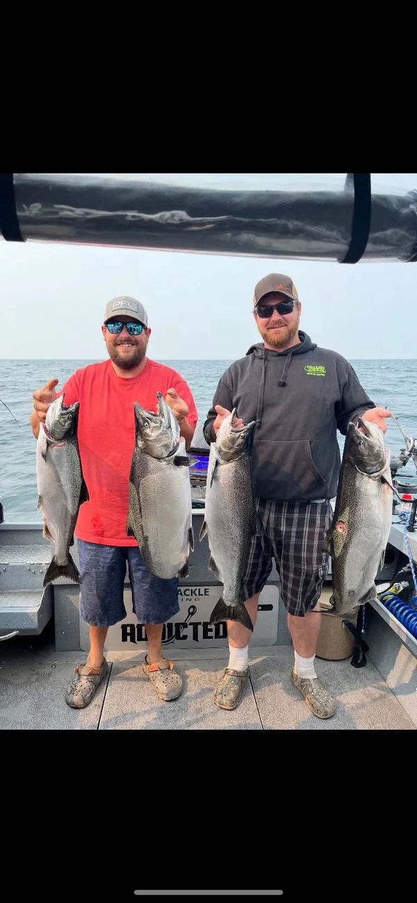 Two men proudly hold large caught fish on a boat at sea.