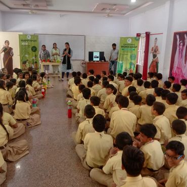 Students seated in a classroom attentively listening to presenters at the front.