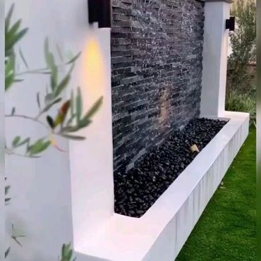 Modern outdoor water feature with black stone wall and white frame.