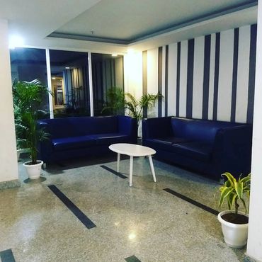 Modern seating area with blue sofas, white round table, and potted plants in a striped wall corner.