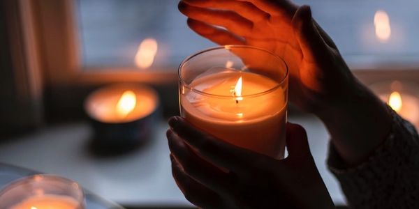 A person holding a candle and protecting it from a breeze next to a window with 3 other candles lit d