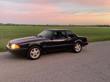 Classic black sports car parked on a rural road at sunset.