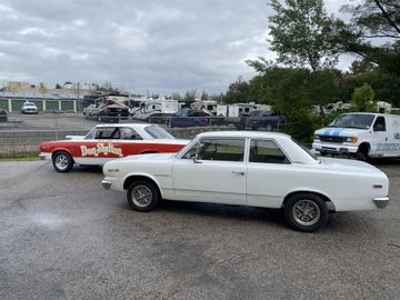 Two vintage cars parked on a wet street under a cloudy sky.