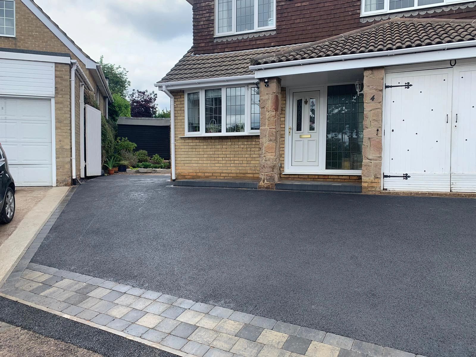 Newly paved driveway outside a house with brick and wood exterior.