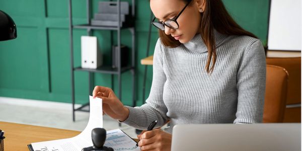 Woman reviewing documents at desk with laptop and charts.