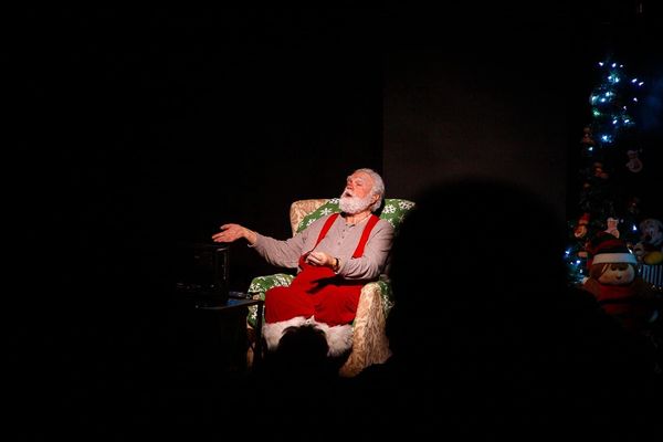 Santa Claus figure sitting and gesturing in a dimly lit room.