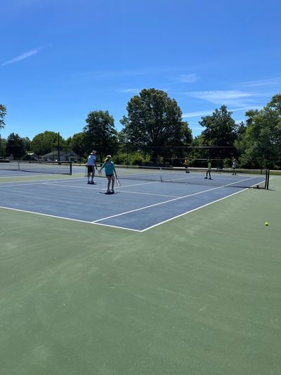 People playing tennis on outdoor courts under a clear blue sky.