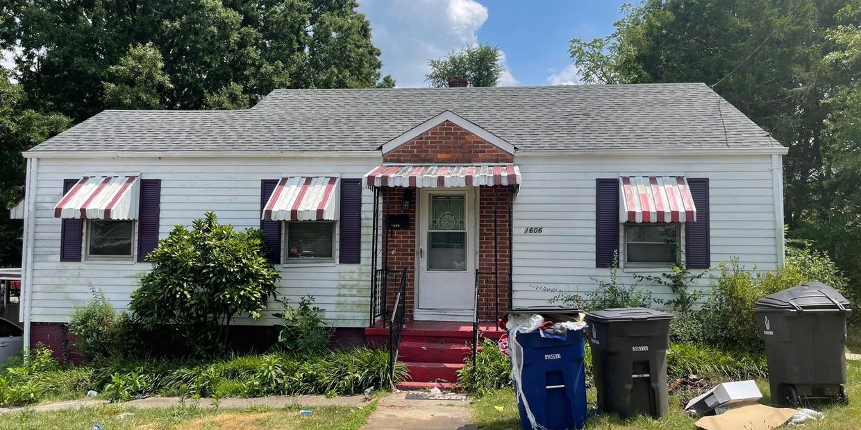 Small white house with striped awnings and trash bins outside.