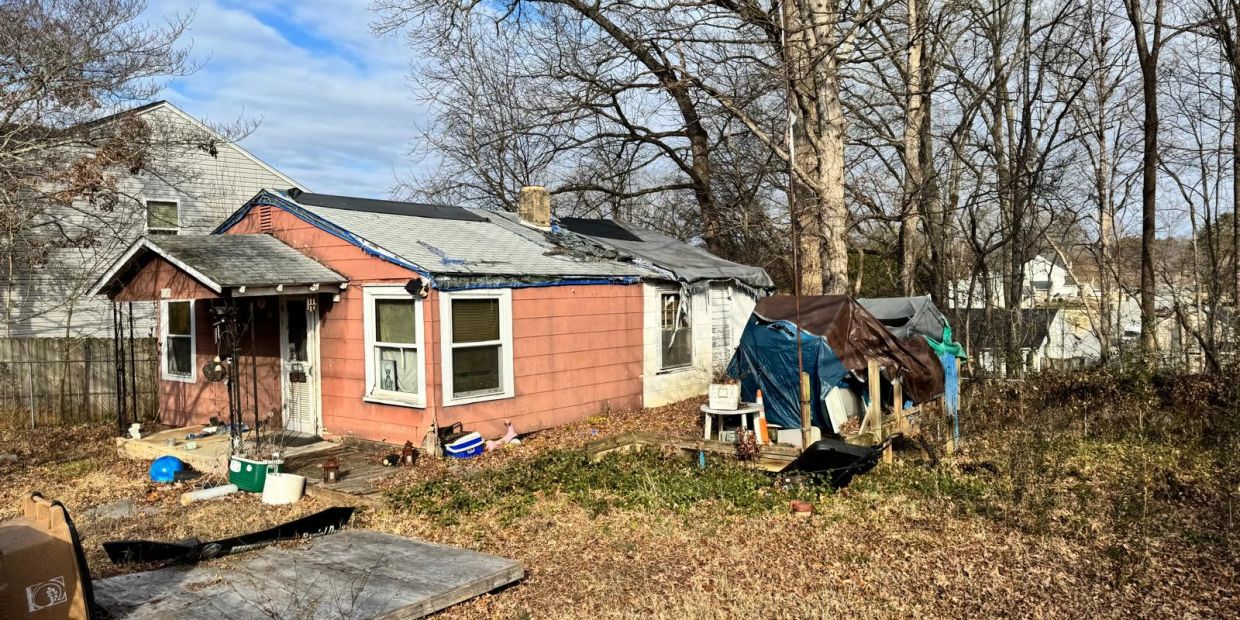 Old pink house with tarp-covered structure in backyard.