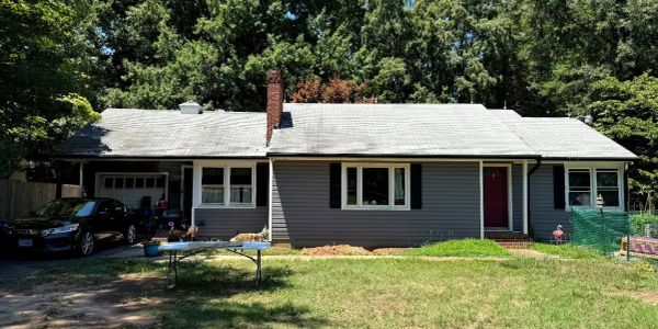 A single-story gray house with a black car parked in the driveway.
