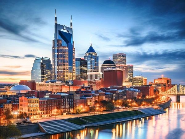 City skyline at dusk with illuminated buildings and river reflections.