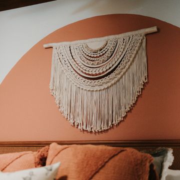 Intricate macrame wall hanging on a terracotta semi-circle accent wall above a cozy bed.
