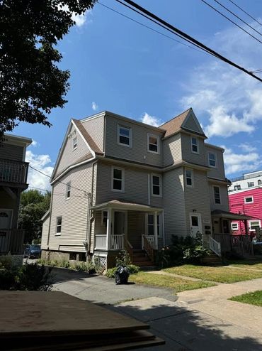 Three-story beige house with a porch and pitched roof.