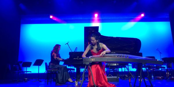 Two women performing on stage with traditional and classical instruments.
