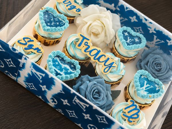 Blue and white cupcakes with floral decorations in a Louis Vuitton-themed box.