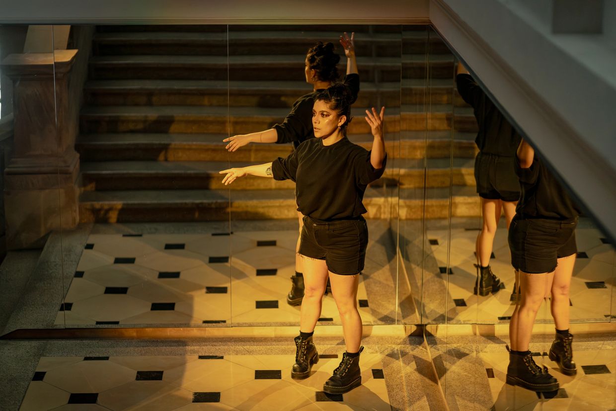 Ámbar de pie en actitud escénica enfrente de una esquina cubierta de espejos grandes que la reflejan