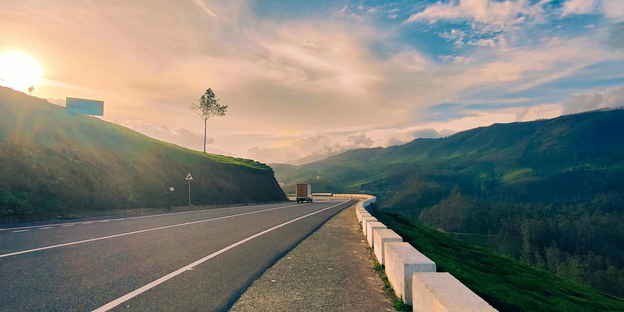Sunset over a winding mountain road with a truck and scenic hills.