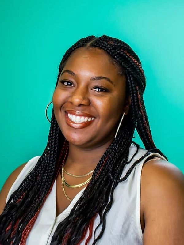 Smiling woman with braided hair against a teal background.